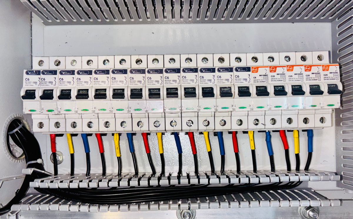 Quadro de distribuição residencial com fileira de disjuntores e fiação separada por cor